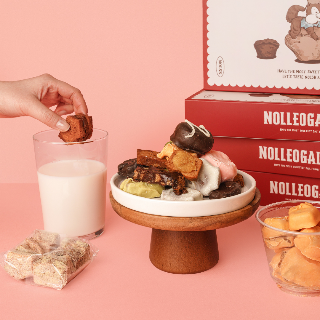 Assorted NOLSK desserts on a wooden stand with a hand dipping a financier into milk
