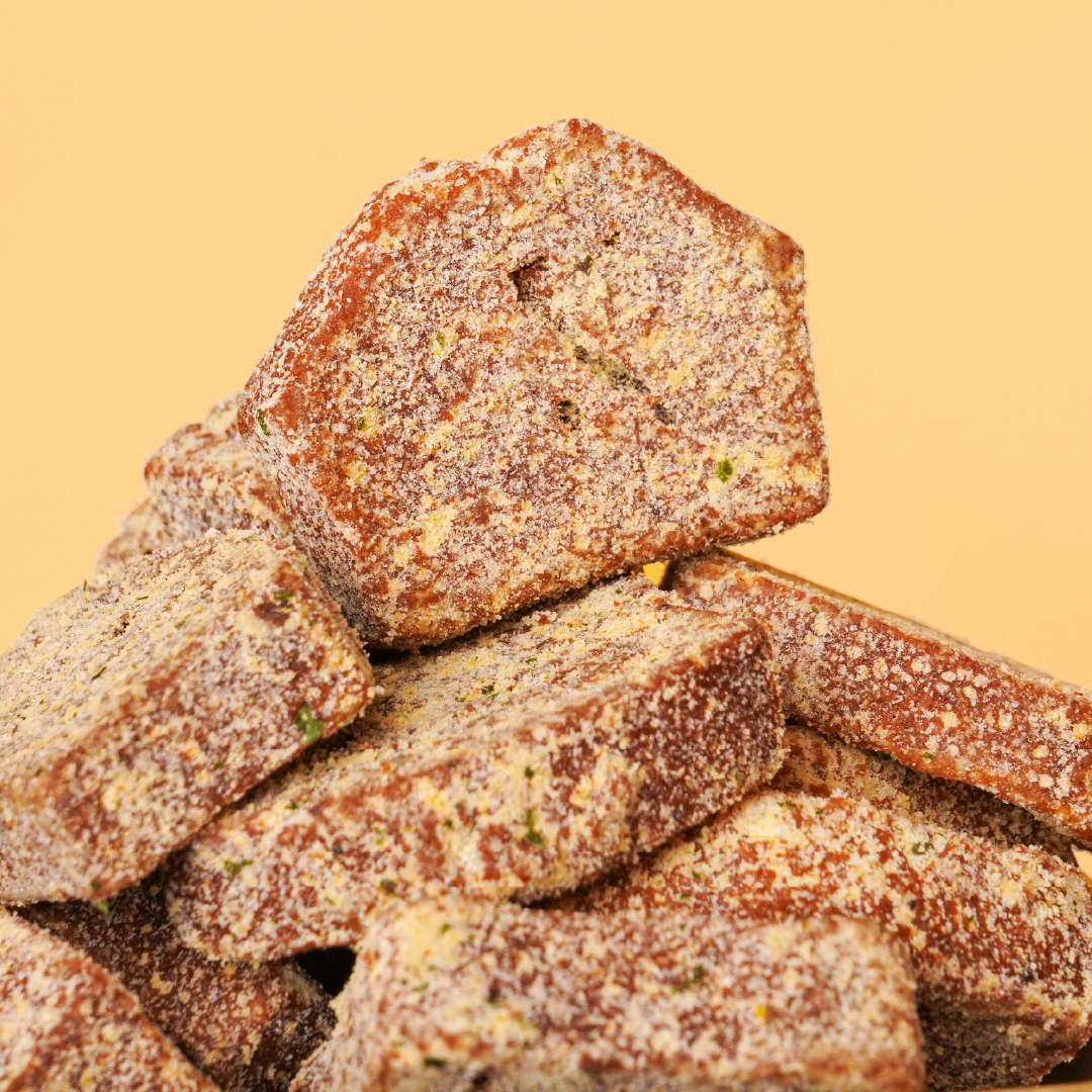 Macro shot of herb-coated NOLSK artisan financier rusk squares against a yellow background